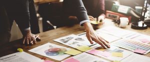 Documents and post-it notes on a desk, with three people's hands scanning across them.
